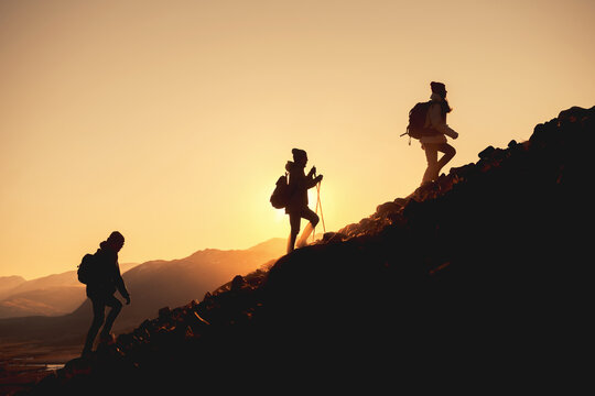 Group of hikers with backpacks walks uphill in sunset mountains