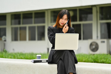 Portrait of Asian woman talking on mobile phone and working with laptop outdoor