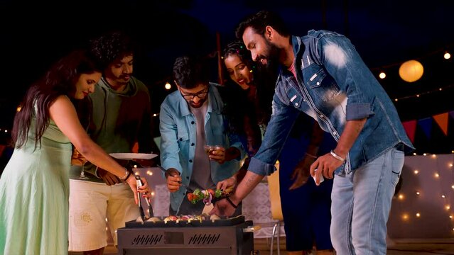 Group of friends busy cooking barbecue grills for dinner during night party - concept of togetherness, birthday gathering and celebration