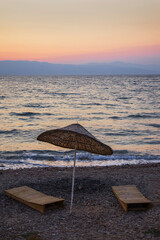 Słomiany parasol oraz leżaki na kamniestej plaży w Turcji. Zachód słońca