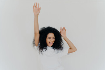 Ecstatic Black woman with curly hair cheering, arms raised, in a white tee
