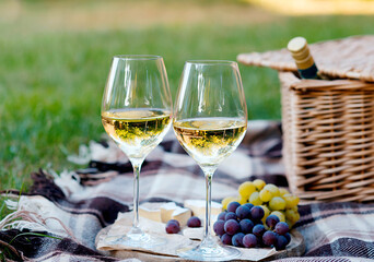 Two glasses of white wine and a wooden plate with cheese and grapes served outside