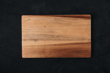Wooden chopping board on dark stone background, top view