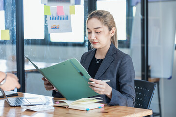 Asian businesswoman working on laptop and financial document paper sitting at desk in office workplace.