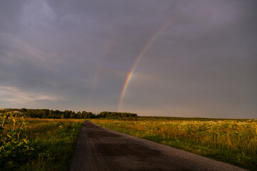 Rainbow over a field road in summer