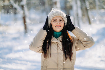 Fototapeta na wymiar Portrait of a beautiful girl in winter clothes standing in a winter park on a sunny day and smiling. The winter vacation. Copy space.