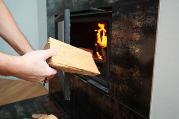 Heating home concept. Mans hand loading firewood into burning fireplace. Solid fuel and heating concept