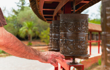 A man's hand spinning a Buddhist prayer wheel, carved with mantras. Buddhist Temple of El Garraf...