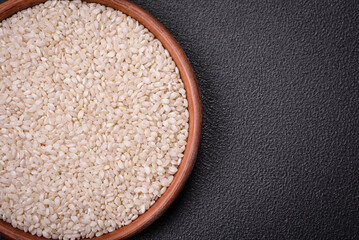 White uncooked rice in a round ceramic bowl on a dark concrete background