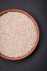White uncooked rice in a round ceramic bowl on a dark concrete background
