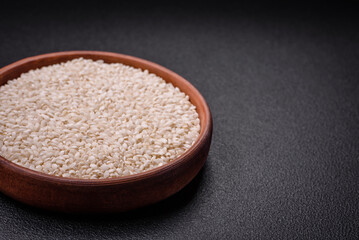 White uncooked rice in a round ceramic bowl on a dark concrete background