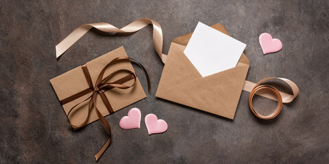 Open brown envelope flat lay with blank card mockup decorated with silk ribbon and silk hearts on dark vintage background. Valentine's Day card. Top view. Banner - obrazy, fototapety, plakaty