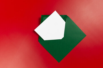 Top view of green envelope, white card on red background. Christmas, New Year composition. Post flat lay, copy space.