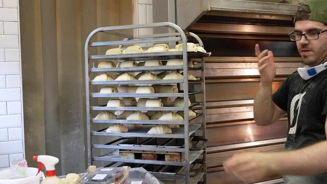 Young baker organizing pre-baked loaves on metal racks before baking in a professional kitchen.