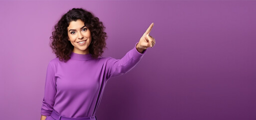 Happy smiling woman with curly hair wearing purple sweater pointing at something with finger...