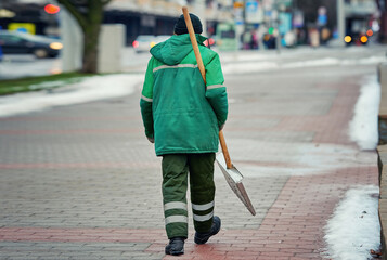 Man with snow shovel ready to clear city street from snow. Utility worker in uniform clean snowy...