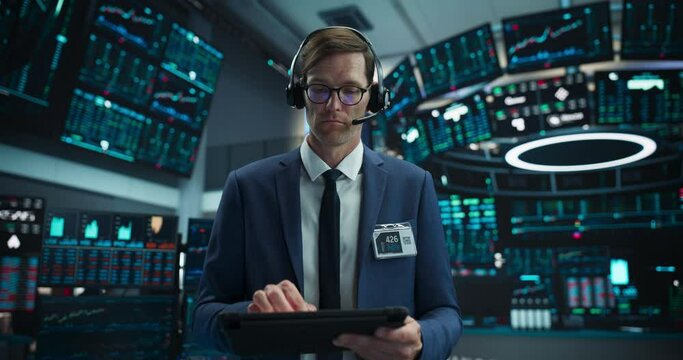 Portrait of a Successful Stock Exchange Manager Wearing Headphones, Working in Modern Office. Proactive Trader Browsing Internet on a Tablet Computer, Using Software with Stock Market Auctions