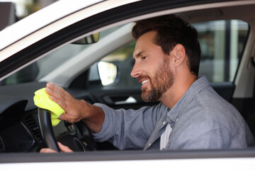 Man cleaning steering wheel with rag in car