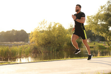 Young man running near pond in park. Space for text