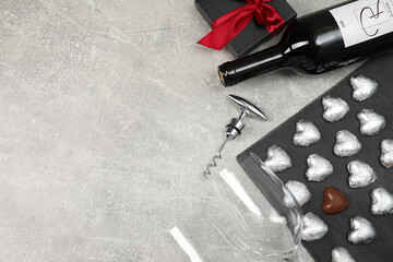 Bottle of red wine, glasses, heart shaped chocolate candies, corkscrew and gift box on light grey...
