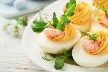 Stuffed or deviled eggs yolk, shrimp, pea microgreens with paprika for easter table decorate fresh cherry or apple blossoms on white light background. Happy Easter traditional dish concept. Mock up.