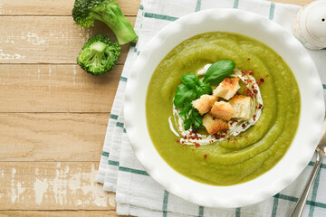 Broccoli cream soup. Fresh homemade broccoli soup in white plate with seasonings, parsley, basil and pieces of toasted bread on rustic white wooden background. Healthy, diet or baby food. Top view.