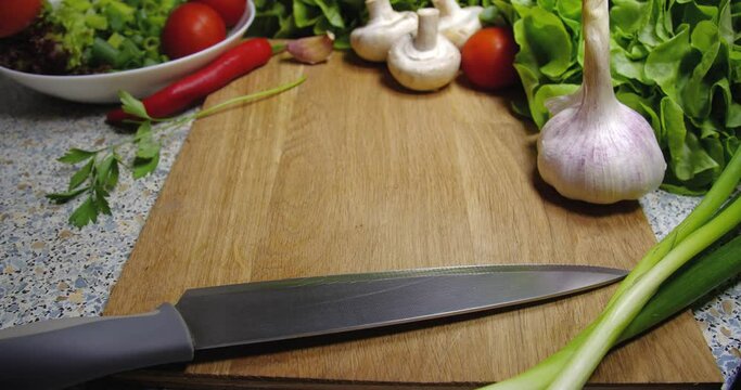  Background close-up of cherry tomatoes lying on a board next to a knife, onion, champignons, garlic and lettuce.Close up human hand taking and putting it.