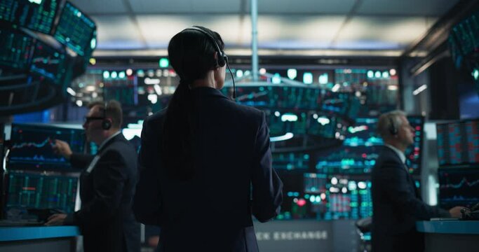 Young Asian Female Broker Working on Tablet Computer on Stock Exchange Floor. Traders Monitoring Real-Time Stocks, Commodities and Exchange Market Data. Professional Investment Agents in Office