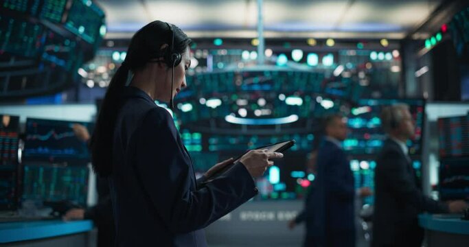 Female Investment Banker Wearing Headphones and Using a Tablet Computer with Financial Market Analytics Data. Team Leader Monitoring Daily Operations, Working of Behalf of Corporate Business Partners