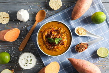Sweet potato puree in bowl, spoon and ingredients on wooden background, top view