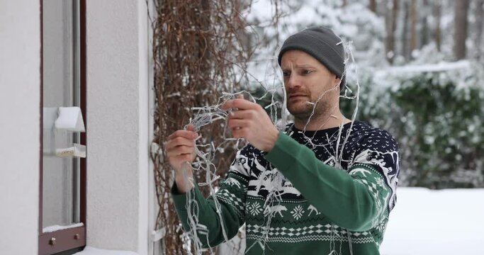 man untangle christmas lights outdoors for house exterior decoration