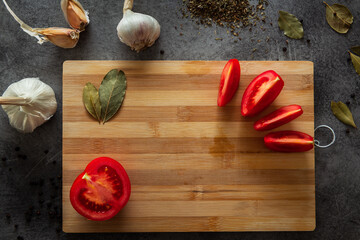 Chopped tomato lies on a wooden cutting board surrounded by herbs and garlic