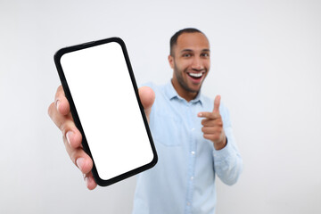 Young man showing smartphone in hand and pointing at it on white background, selective focus. Mockup for design