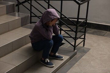 Child abuse. Upset boy sitting on stairs indoors