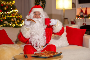 Obraz na płótnie Canvas Merry Christmas. Santa Claus with cup of drink and pizza watching TV on sofa at home