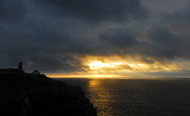 Cloudy and golden sunset at Cape San Vicente with the silhouette of the lighthouse on the cliffs. Cape Saint Vincent is in Algarve, Portugal, the most extreme geographical point in southwestern Europe