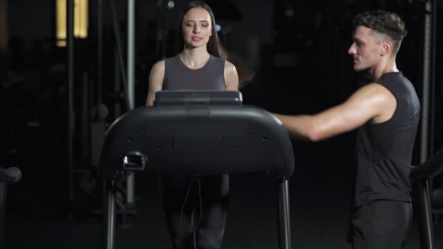 Young woman running on a treadmill, training with a coach, perform aerobic exercise and endurance training in the gym, nightlife.