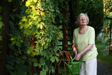 pensioner blond woman with water can on beautiful garden background close up photo