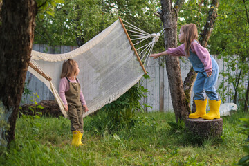 Two children playing near a hammock; a serene garden scene. Depicts the value of outdoor play in child development.