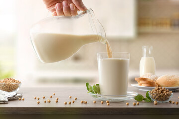 Filling glass with soy milk from a jug in kitchen