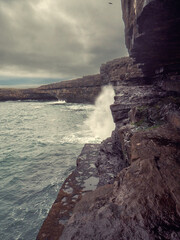 Rough stone coast and cliff of Aran Island, county Galway, Ireland. Nobody. Cloudy sky. Irish nature scene landscape. Dark and dramatic mood. Dún Aonghasa fort in the background.