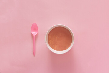Top view of pink spoon and white deep plate with pudding on a pink pastel background. Minimal...