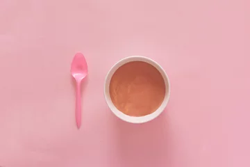 Foto op Aluminium Top view of pink spoon and white deep plate with pudding on a pink pastel background. Minimal holiday or food concept. © Aleksandar