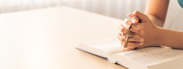 Cropped image of female reading a bible book while holding cross at wooden table with blurring...