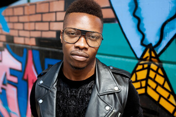 Portrait of a young african handsome man in glasses and afro hairstyle, posing against graffiti...