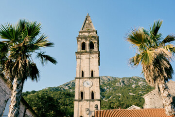 Bell tower of the Church of St. Nicholas against the backdrop of green mountains and blue sky. Perast, Montenegro