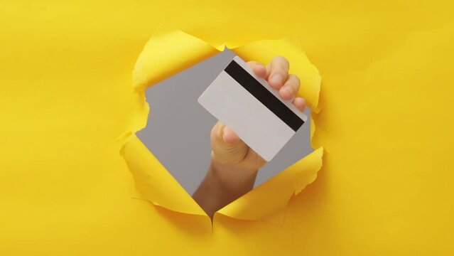 Woman hand holding credit bank card isolated through torn yellow background copy space for bank advertisement place for text or image promotional content.