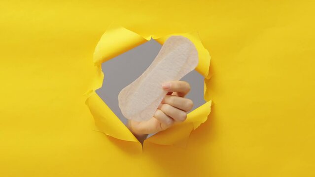 Period protection with cotton. Disposable menstrual product. Intimate and feminine care. Unrecognizable human hand showing cotton pad breaking trough yellow free space paper