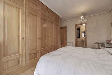 Large built-in wardrobe in the bedroom with oak wood doors, double bed, access to a bathroom,...