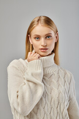 portrait of blonde woman in white knitted sweater and natural makeup looking at camera on grey